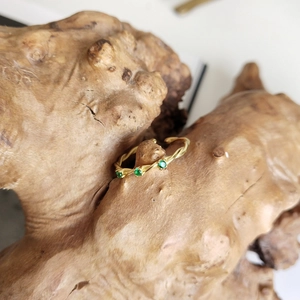 Detail of a vintage twisted gold ring set with three green stones on rustic wood