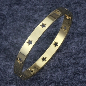 Detail of gold-plated star hollow-out bangle with secure side clasp on dark fabric