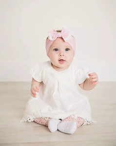 Close-up of a baby girl wearing a soft pink nylon headband with a large lace bow.