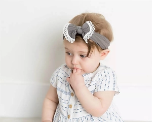 Close-up of a baby wearing a soft gray nylon headband with a lace-trimmed bow