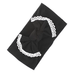 Detail view of a black nylon baby headband featuring a large bow with white lace trim.