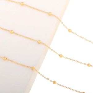 Detailed close-up of golden beaded eyewear chain with smooth matte spheres and fine metal links