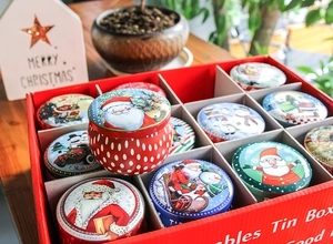 Detailed view of Christmas tin containers set with Santa and snowman patterns in a red gift box