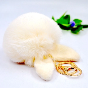Close-up of a soft cream fluffy pompom keychain with cute bunny ears and gold metal clasp