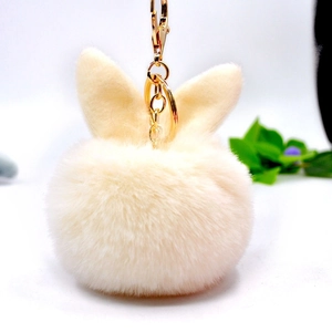 Close-up of fluffy cream plush bunny ear pompom keychain with golden metal ring and clasp