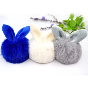 Detailed close-up of fluffy plush pom-pom charms with rabbit ears in blue, beige, and grey