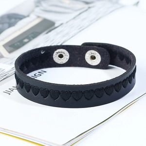 Detail of black leather bracelet with heart embroidery and snap button on magazine