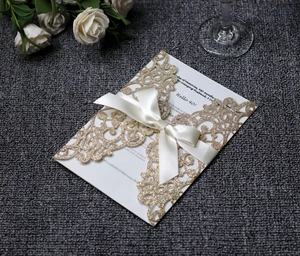 Detail of laser-cut gold glitter invitation featuring a white silk ribbon bow and texture