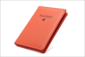 Macro shot of orange leather passport holder with black engraved text and aircraft motif