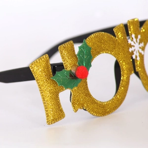 Close-up of glittery gold HO letters with holly leaves on festive Christmas party glasses