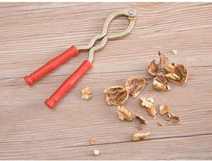Top-down view of metal nutcracker with red handles on wood background with walnut shells