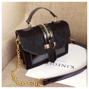 Detail of black suede and patent leather handbag with gold metal handle and chain strap