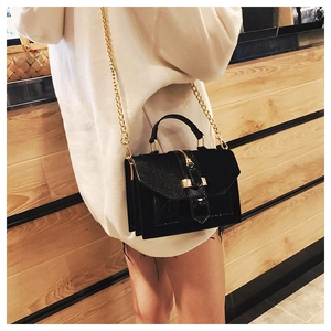 Detail of black crossbody bag with shimmering flap, golden chain, and buckle on model