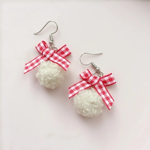 Detail of red plaid bow earrings with soft white plush pompoms and metallic hooks