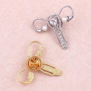 Stylized uterus-shaped brooches in gold and silver finish with pearls and crystals