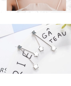 Detail of silver long drop earrings with cubic zirconia and star charms on a ceramic plate
