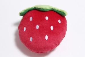 Top down macro view of strawberry plush dog toy showing red fabric and green leaf detail