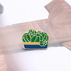 Macro view of green cactus enamel brooch with gold trim on a minimalist background