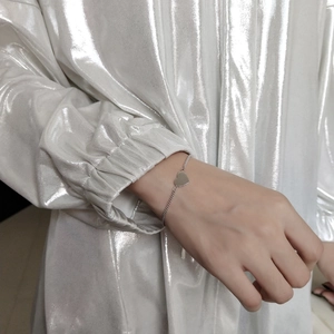 Detailed view of a silver minimalist heart charm bracelet worn on a female wrist