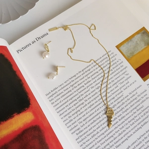 Detail of vintage gold key necklace and irregular pearl earrings on art magazine