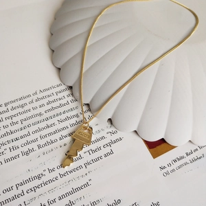 Close-up of a gold key pendant necklace featuring engraved number on shell tray