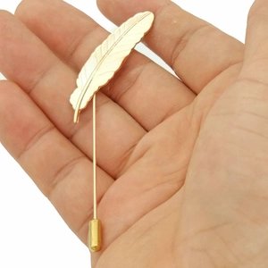 Detail of golden alloy feather lapel pin showing textured metal leaf patterns and stick pin