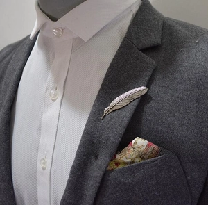 Detailed silver feather brooch pin on a dark grey suit lapel for professional styling