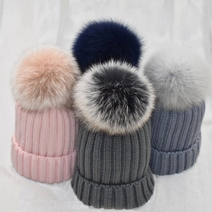 Detailed view of knitted hats featuring fluffy pom-poms and thick ribbed texture cuffs