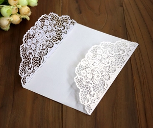 Intricate laser-cut lace pattern on a white wedding invitation envelope over wood