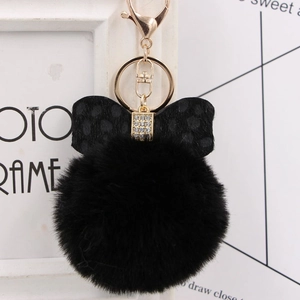 Detail of a fluffy black faux fur pompom keychain with a leopard print bow and gold clip