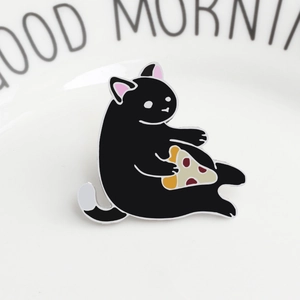 Detail of creative black cat enamel pin with pizza on a white ceramic breakfast plate