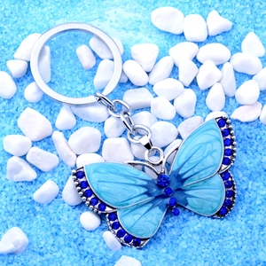 Close-up of blue butterfly keychain with rhinestones on blue sand and white pebbles