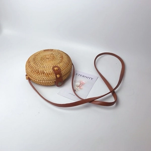 Detailed macro view of the circular woven rattan bag with brown leather strap and buckle