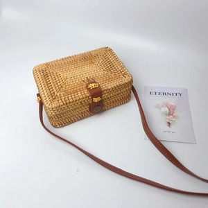 Detail view of a handmade rectangular rattan bag with brown leather strap on white surface