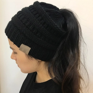 Detail view of black knit ponytail beanie with soft wool texture and leather patch
