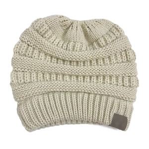 Close-up of cream knit ponytail beanie showing thick texture and grey label detail