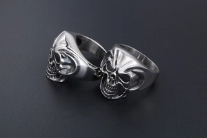 Close-up of two polished silver titanium steel skull rings for men with ghost face detail
