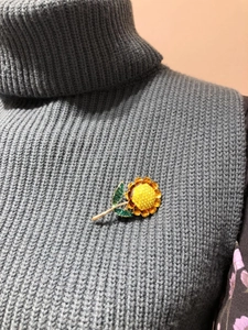Detail of sunflower brooch with yellow and green crystals on a grey knit sweater