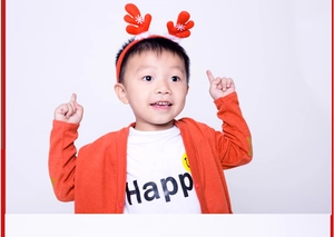 Close-up of a smiling child wearing a red reindeer antler headband with white snowflakes