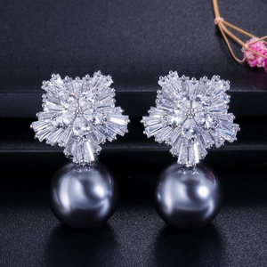 Detail of snowflake zircon earrings with a dark grey pearl drop on a textured background