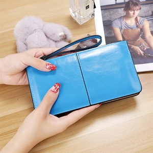Blue long leather wallet held by hands over a wooden table with lifestyle accessories