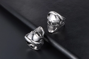 Detailed view of silver skull rings with headphones on black textured leather surface