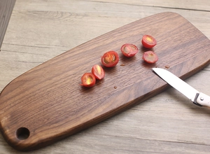 Detail of dark walnut cutting board with round handle hole on light wood background