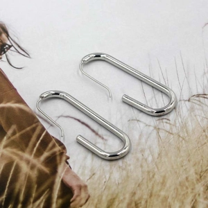 Orecchini geometrici a forma di U in ottone argento su sfondo di rivista di moda
