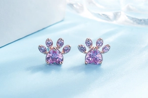 Macro shot of rose gold cat paw earrings with pink heart gemstones on blue silk background