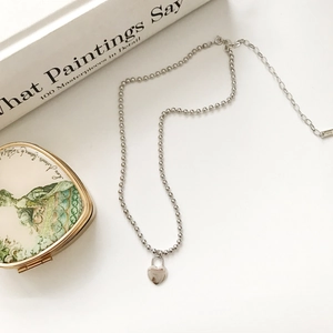 Macro shot of silver bead chain necklace featuring a heart lock pendant and lobster clasp