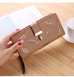 Close-up of a long brown wallet with leaf-pattern cutouts and a gold leaf metal charm