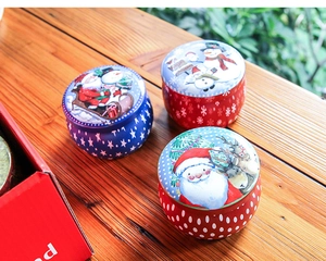 Three festive Christmas tin cans featuring Santa and reindeer on a rustic wood surface