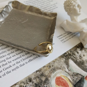 Detailed view of an oval gold adjustable ring on a metal tray with artistic props