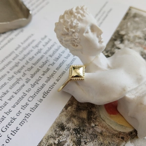 Macro shot of gold square pyramid ring with beaded edges on artistic prop